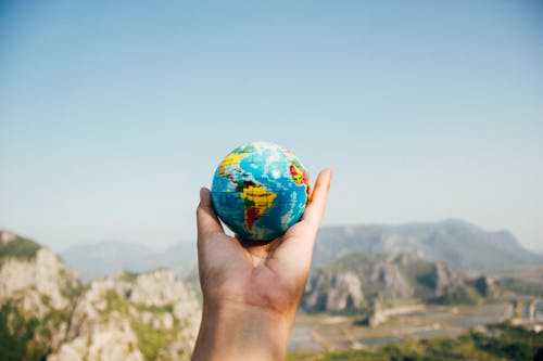 Free Person Holding World Globe Facing Mountain Stock Photo