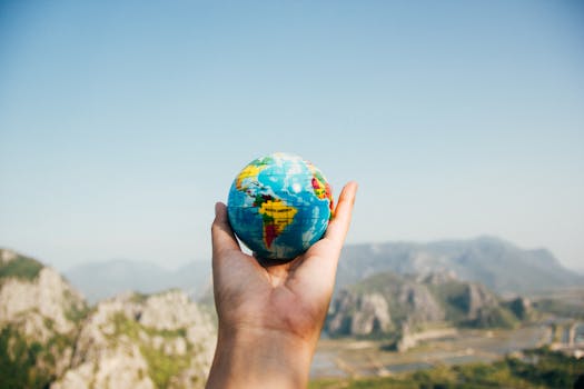 Person Holding World Globe Facing Mountain