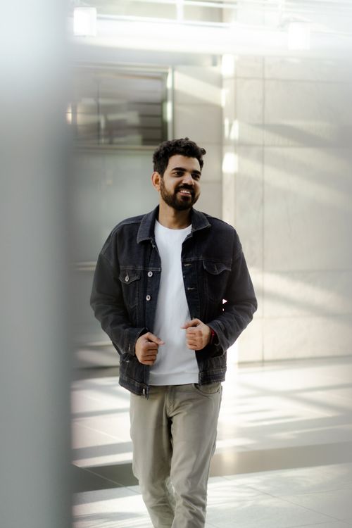 Free A casually dressed man smiles while walking indoors, bathed in soft light. Stock Photo