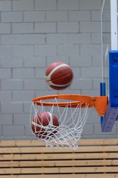 Two basketballs seen scoring through a hoop on an indoor court, emphasizing sports action.