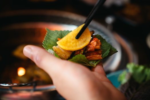 Korean BBQ leaf wrap showcasing daikon, kimchi, and pork belly in an intimate dining setting.