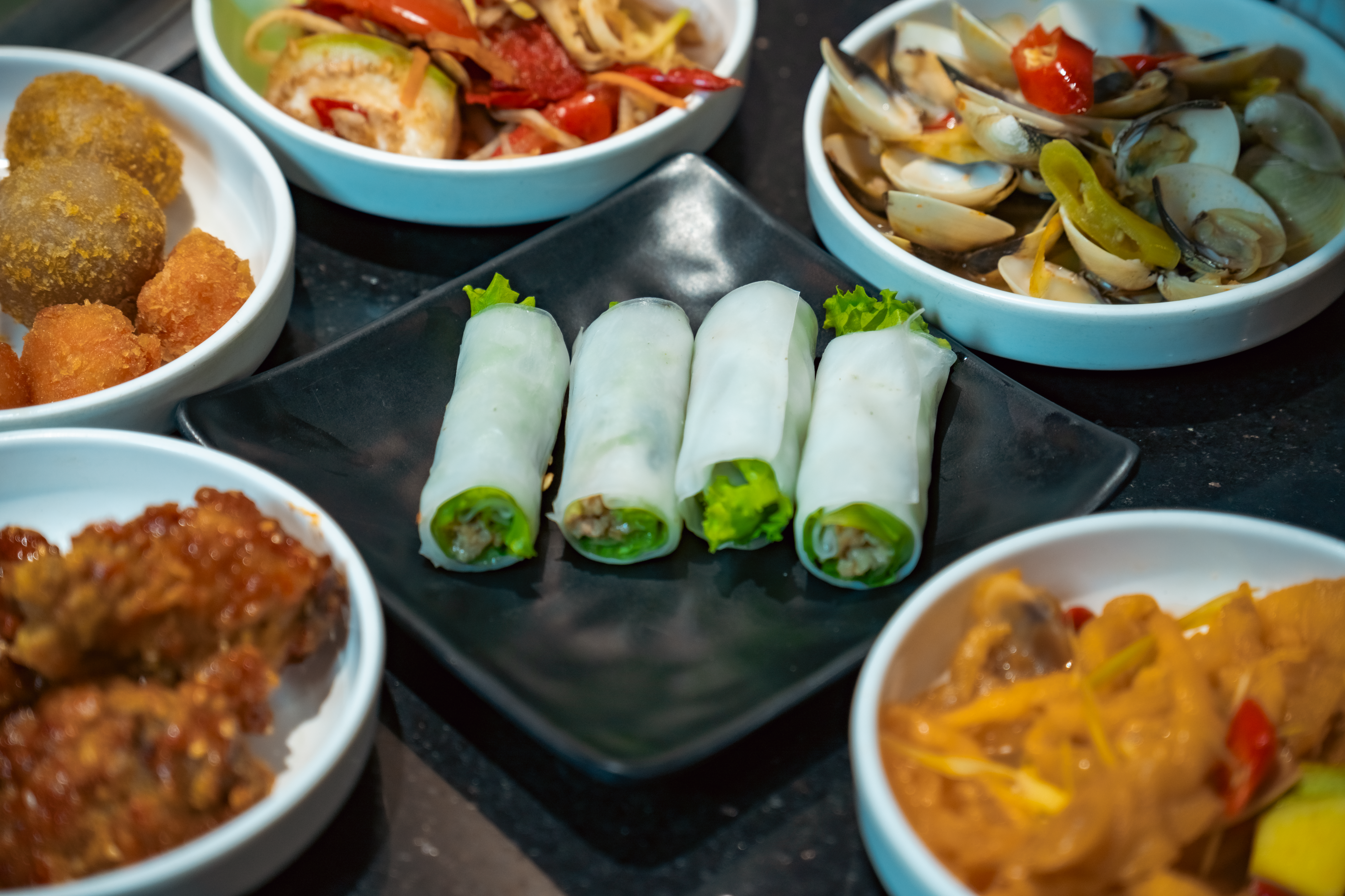 Pictured is a variety of delicious Asian dishes including fresh spring rolls, fried appetizers, and seafood.