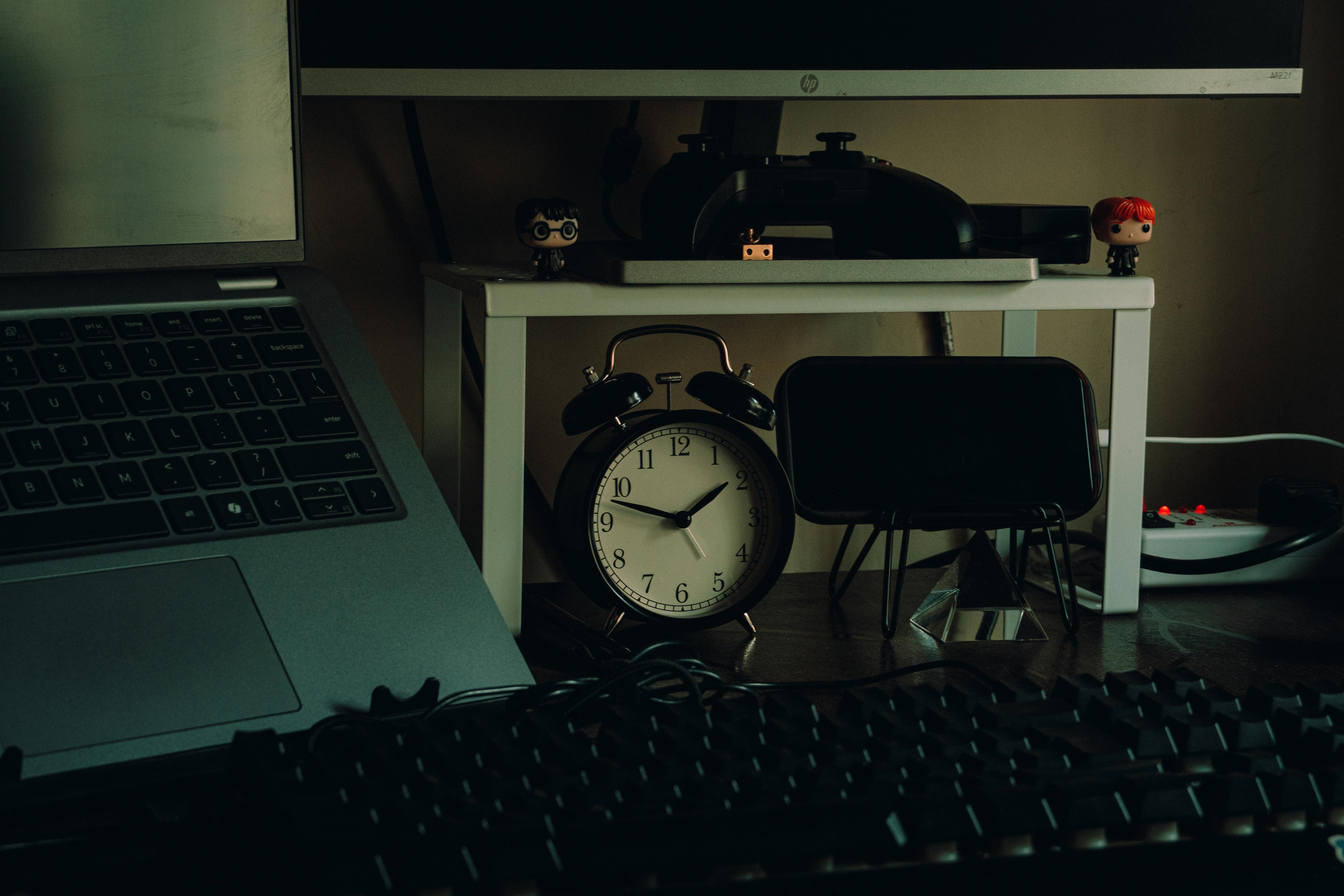 Tidy desk setup with a laptop, analog clock, and desk decor in a modern home workspace setting.
