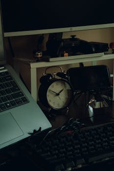 A cozy home office setup featuring a vintage analog clock and modern tech on a wooden desk.
