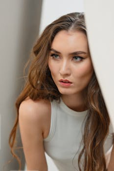 Close-up portrait of a woman with long brown hair in a white top, looking pensive.
