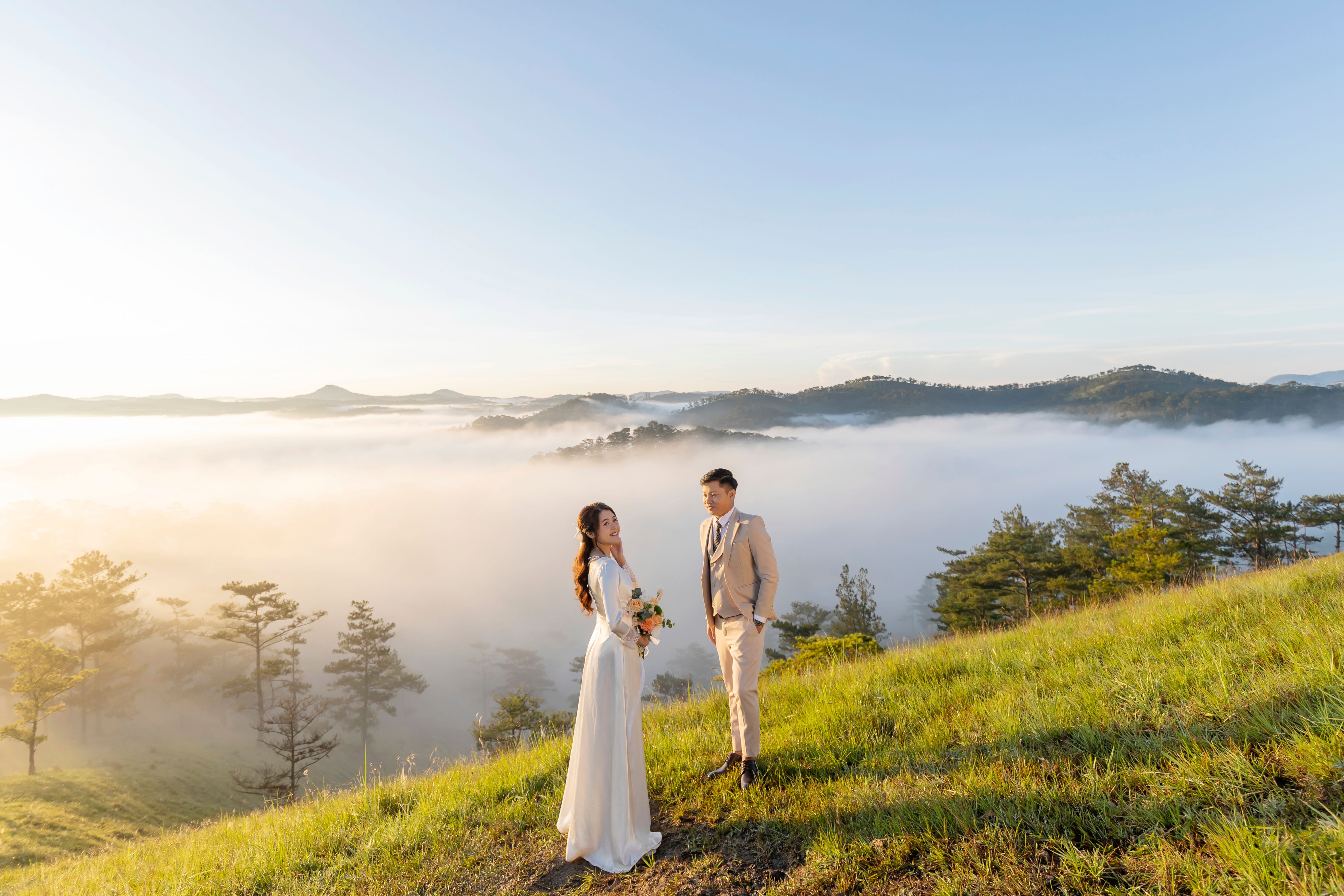 Couple standing on hilltop amidst misty mountains, capturing a romantic moment.