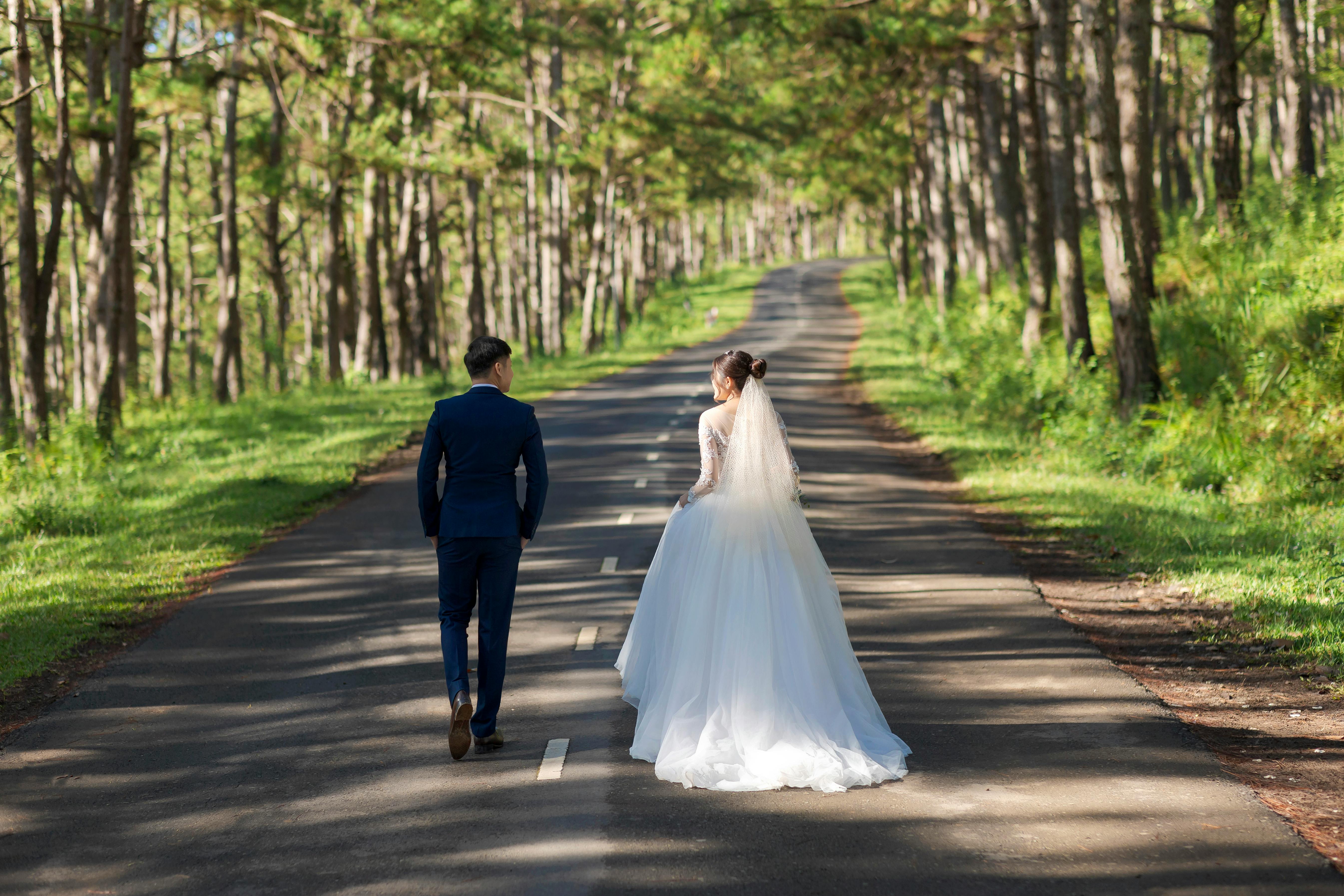 A bride and groom walk along a tree-lined road, symbolizing a journey into their new life together.