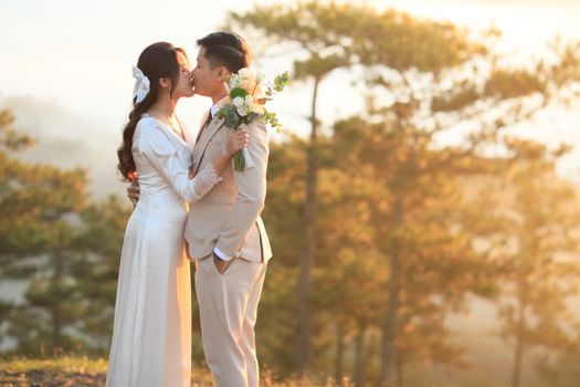 A bride and groom share a romantic kiss during their outdoor wedding at sunset.