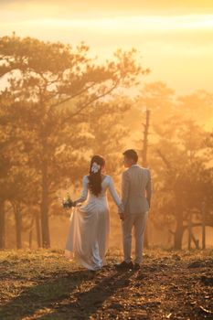 A couple in wedding attire strolls through a sunlit forest, adding magic to the serene landscape.
