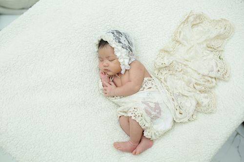 Free A newborn baby peacefully sleeping in a soft white lace wrap on a plush blanket. Stock Photo
