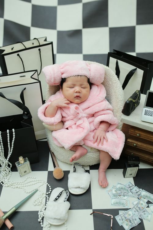 Free Adorable baby in pink robe amidst luxury shopping bags and accessories. Stock Photo