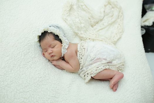 Adorable newborn baby sleeping peacefully in a soft, lace outfit on a cozy blanket.