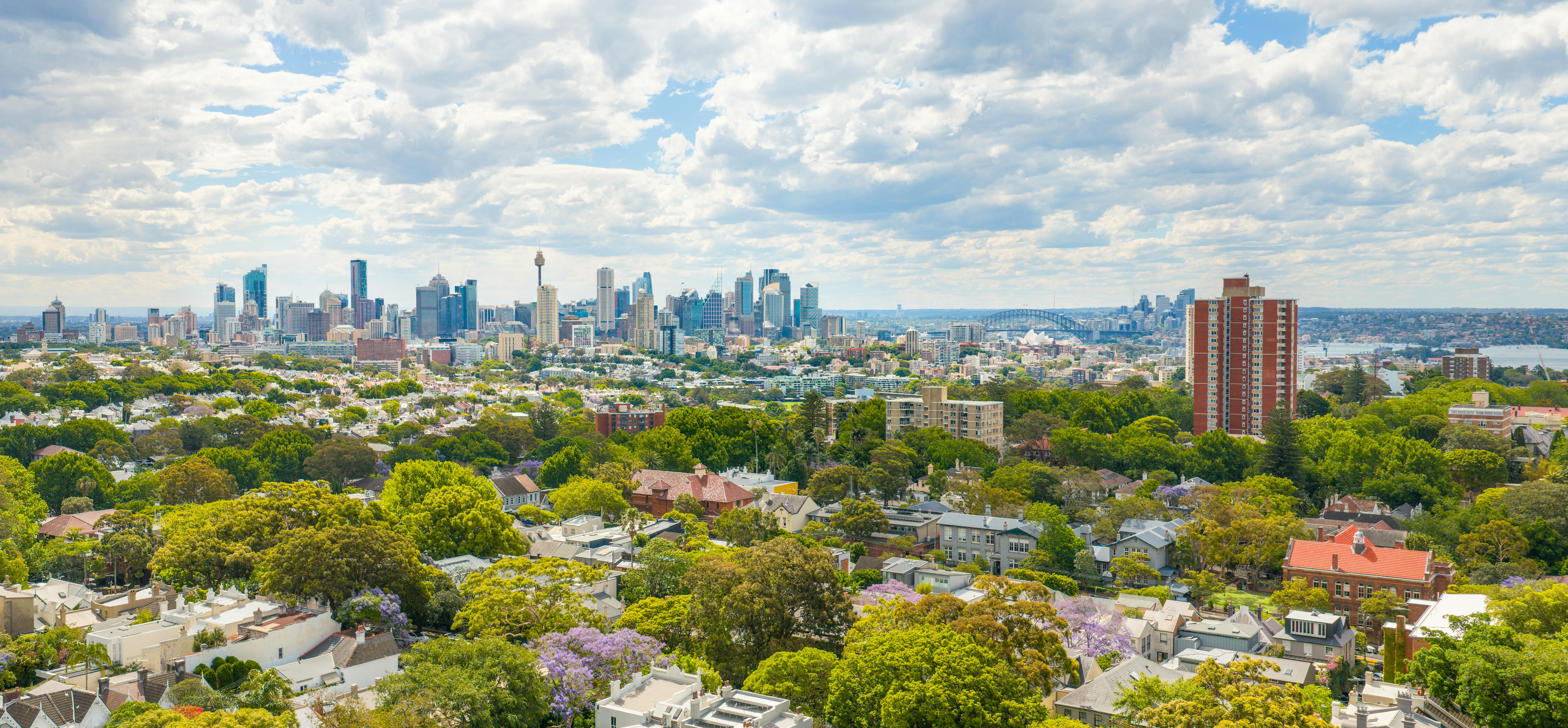 A stunning aerial view of Sydney's skyline with lush greenery in the suburbs, featuring iconic landmarks and vibrant city life.