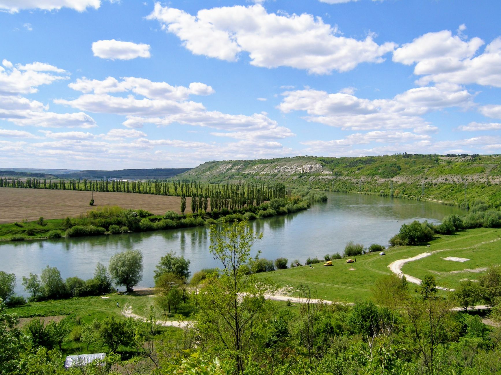 A winding river flows through a green landscape under a bright blue sky.