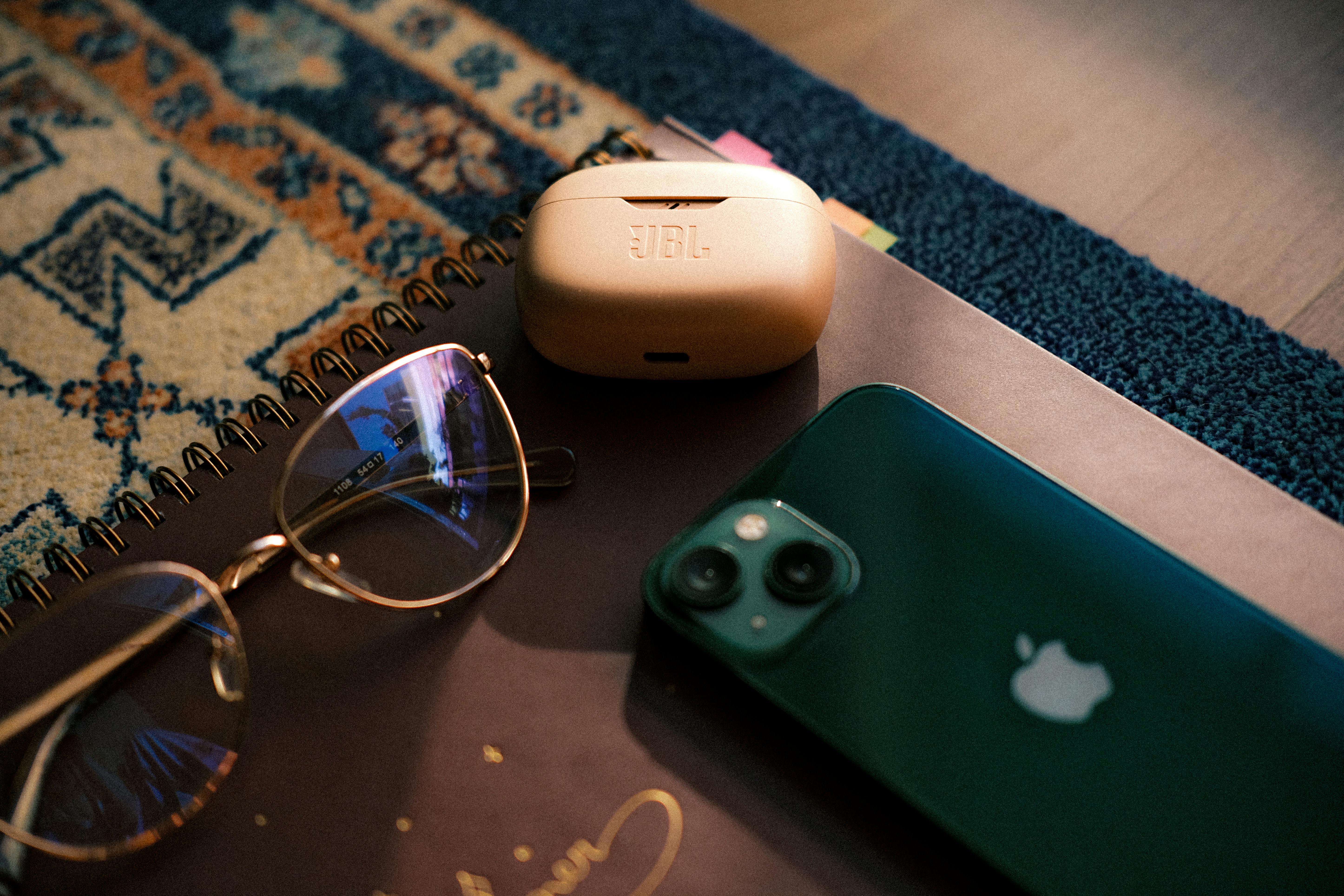 Gratis Composición plana de gafas, teléfono inteligente, auriculares y cuaderno sobre una alfombra estampada. Foto de stock