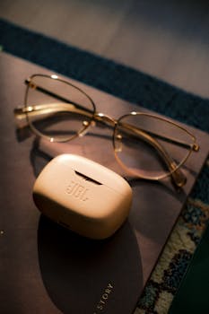 A pair of glasses and JBL headphones rest on a notebook under warm lighting, creating a cozy ambiance.