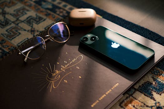 Stylish desk setup featuring notebook, sunglasses, smartphone, and headphones in soft natural lighting.