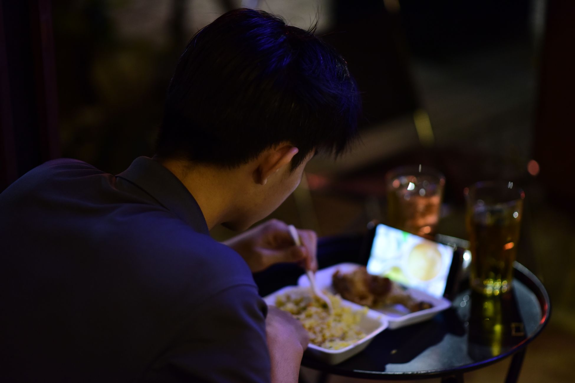 A young adult enjoys a meal while watching a video on their smartphone, creating a cozy night scene.