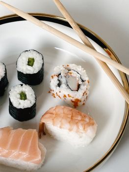A close-up of assorted sushi rolls and nigiri on a plate with chopsticks.