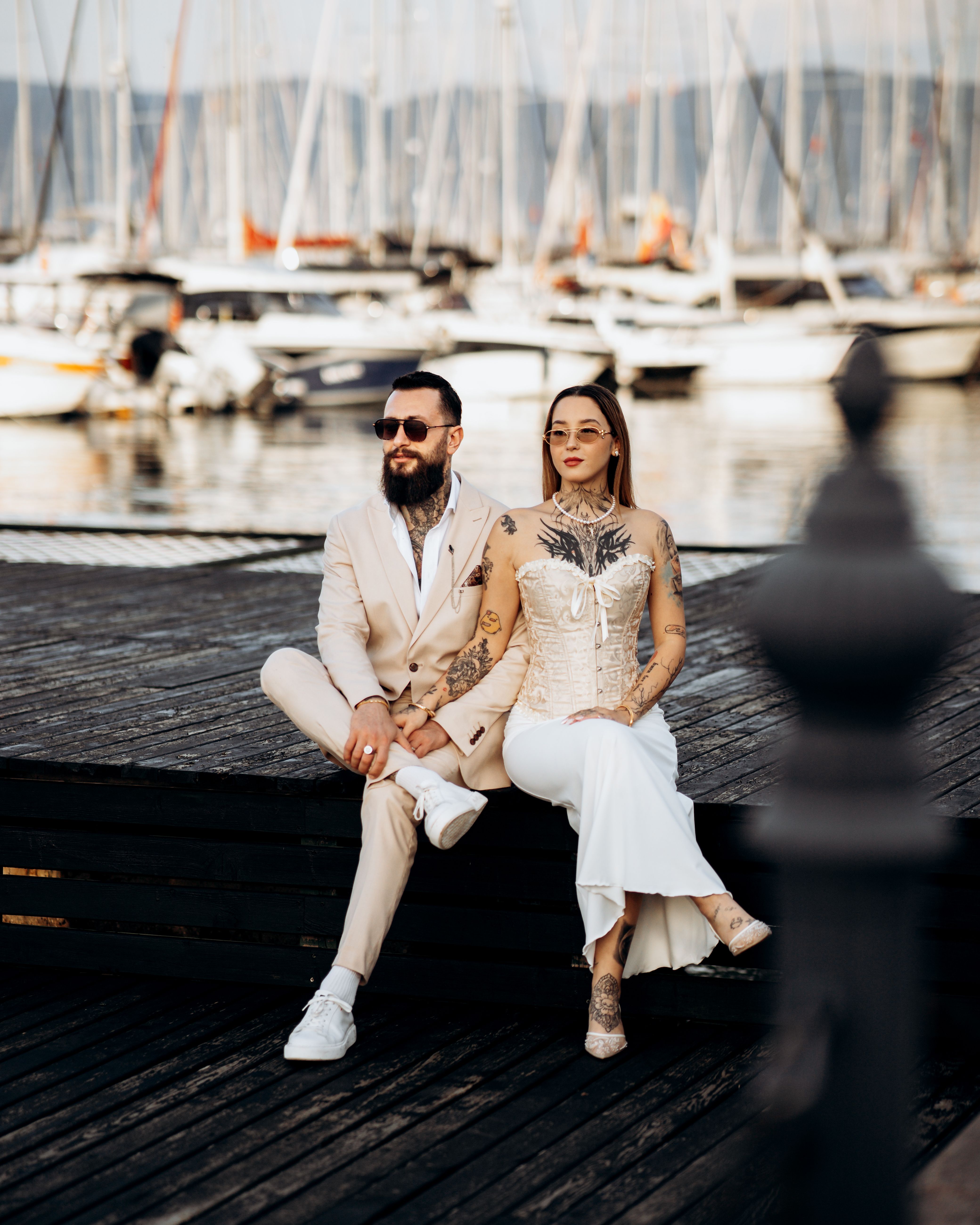 Fashionable couple with tattoos relaxing by a marina, exuding style and elegance.