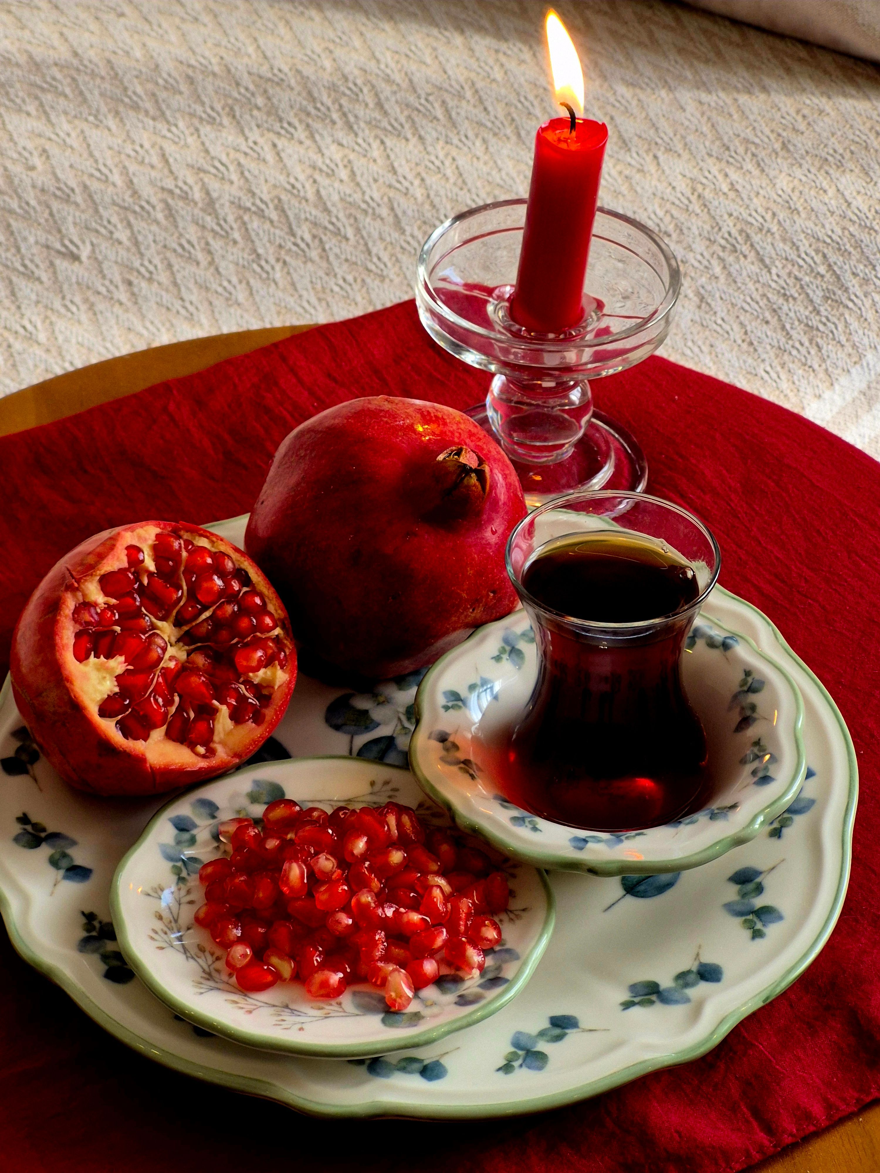 A still life featuring pomegranates, tea, and a lit candle creating a warm, inviting scene.