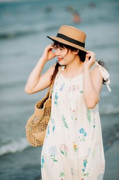 A young woman in a floral dress and hat enjoys a sunny day walk along a coastal beach.