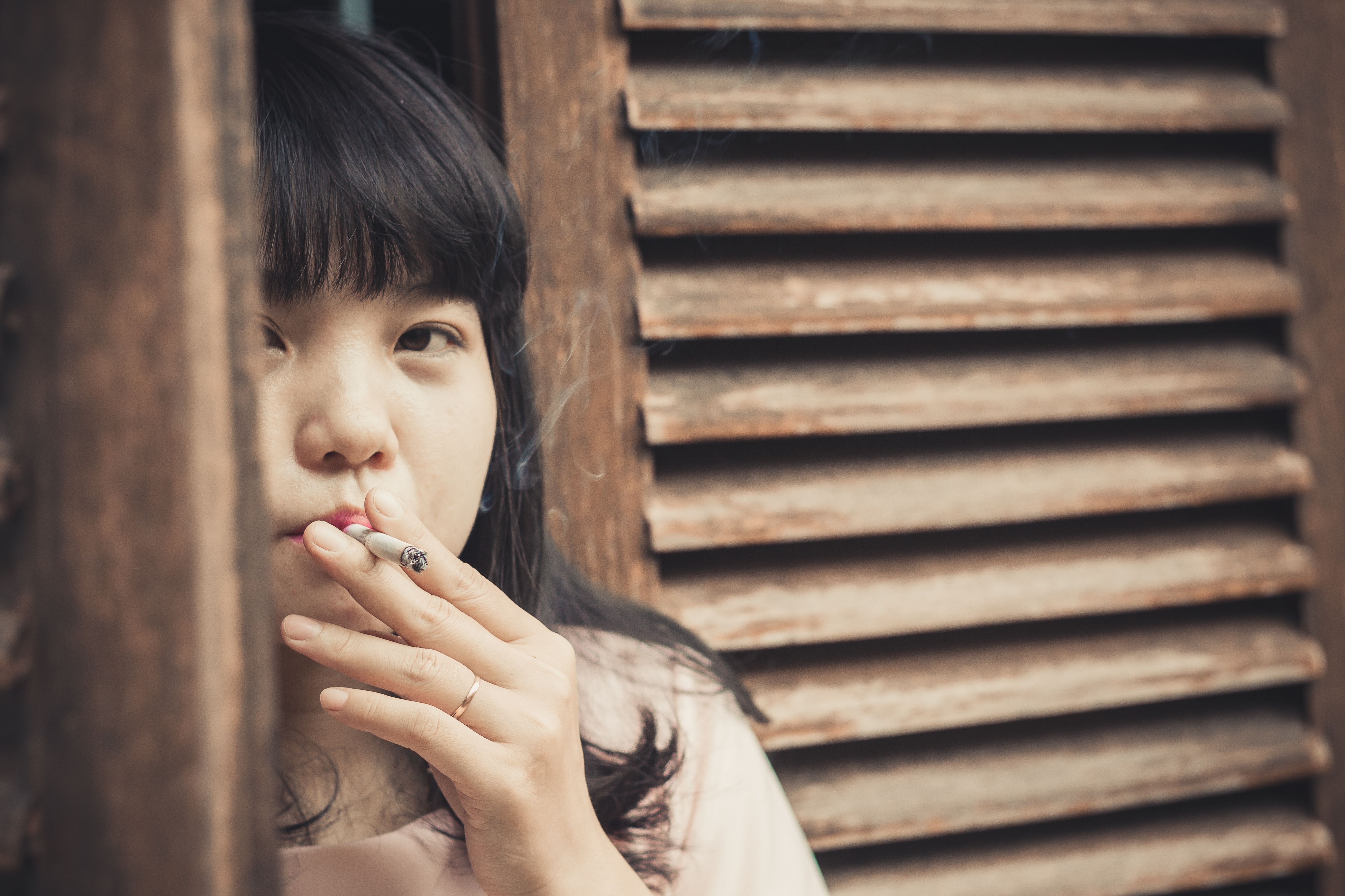 Contemplative Woman Smoking by Wooden Shutters · Free Stock Photo