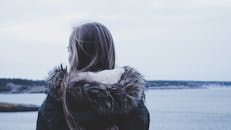 冬日严寒，一名身着毛皮夹克的女子凝望大海，营造出宁静而沉思的氛围