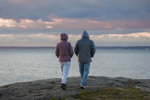 Free A couple walks on the rocky shore of Stamford, Connecticut during sunrise, enveloped in autumn tranquility. Stock Photo