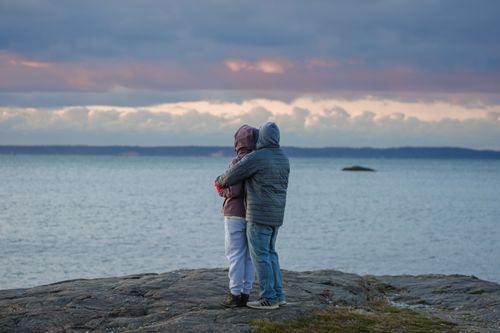 Free A couple warmly embraces at dawn by the shoreline at Stamford's Cove Island Park in autumn. Stock Photo