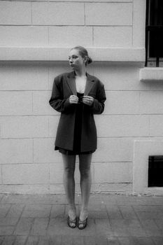 Stylish woman in oversized blazer posing against a wall in a monochrome shot.
