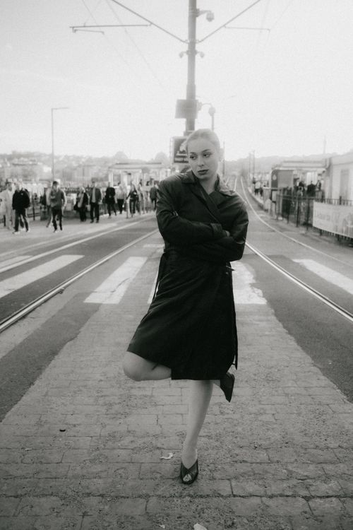 Free Black and white photo of a fashionable woman standing confidently on tram tracks in a city, exuding urban style. Stock Photo