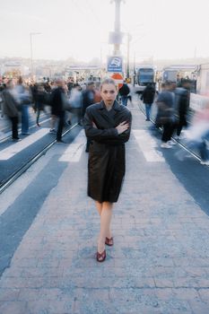 A stylish woman stands confidently amidst blurred pedestrians in a busy cityscape.