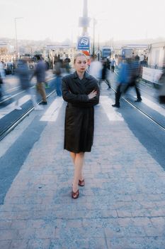 A woman in a coat stands still amidst a blurred crowd on a city street, creating a dynamic contrast.