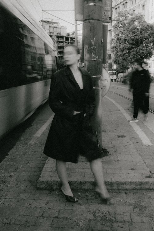 Free A black and white photo of a blurred woman standing on a busy urban street with a moving tram. Stock Photo