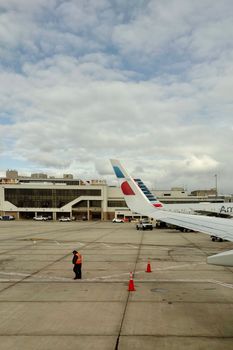 View of airplane wing and ground crew at airport under cloudy sky.