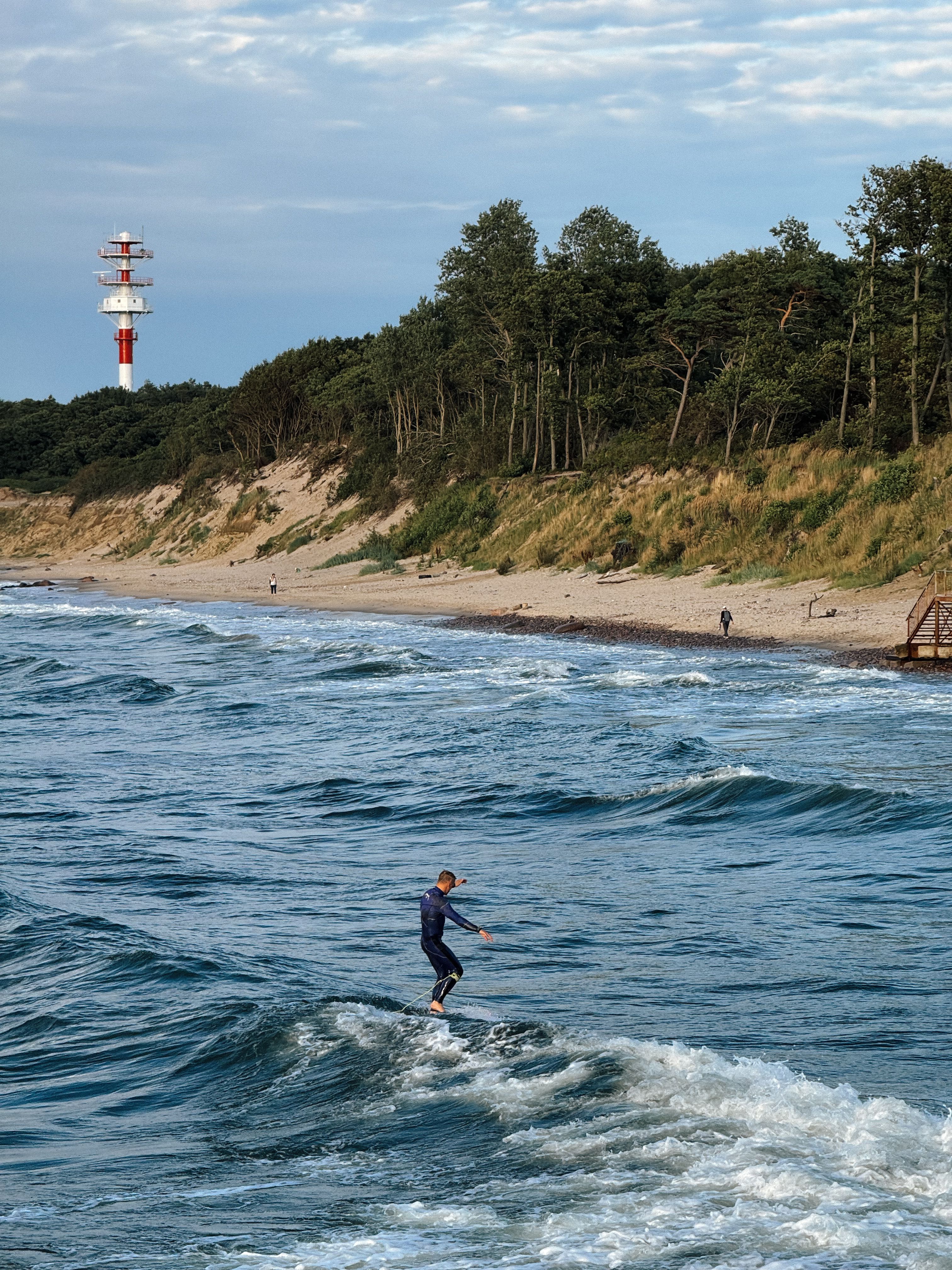 Surfer catching waves near a lighthouse on a scenic coastline.