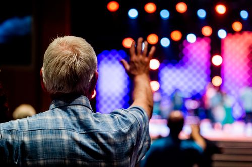 Free Senior man enjoying a concert with vibrant stage lights and a lively atmosphere. Stock Photo