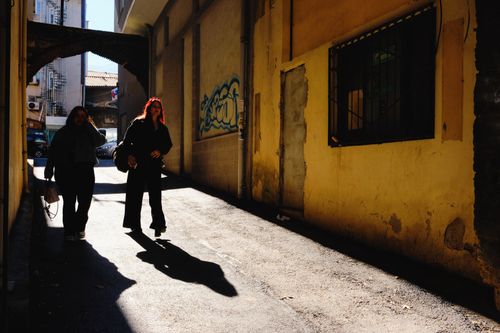 Free Two people casting shadows while walking down a vibrant alley in Bursa, Türkiye. Stock Photo