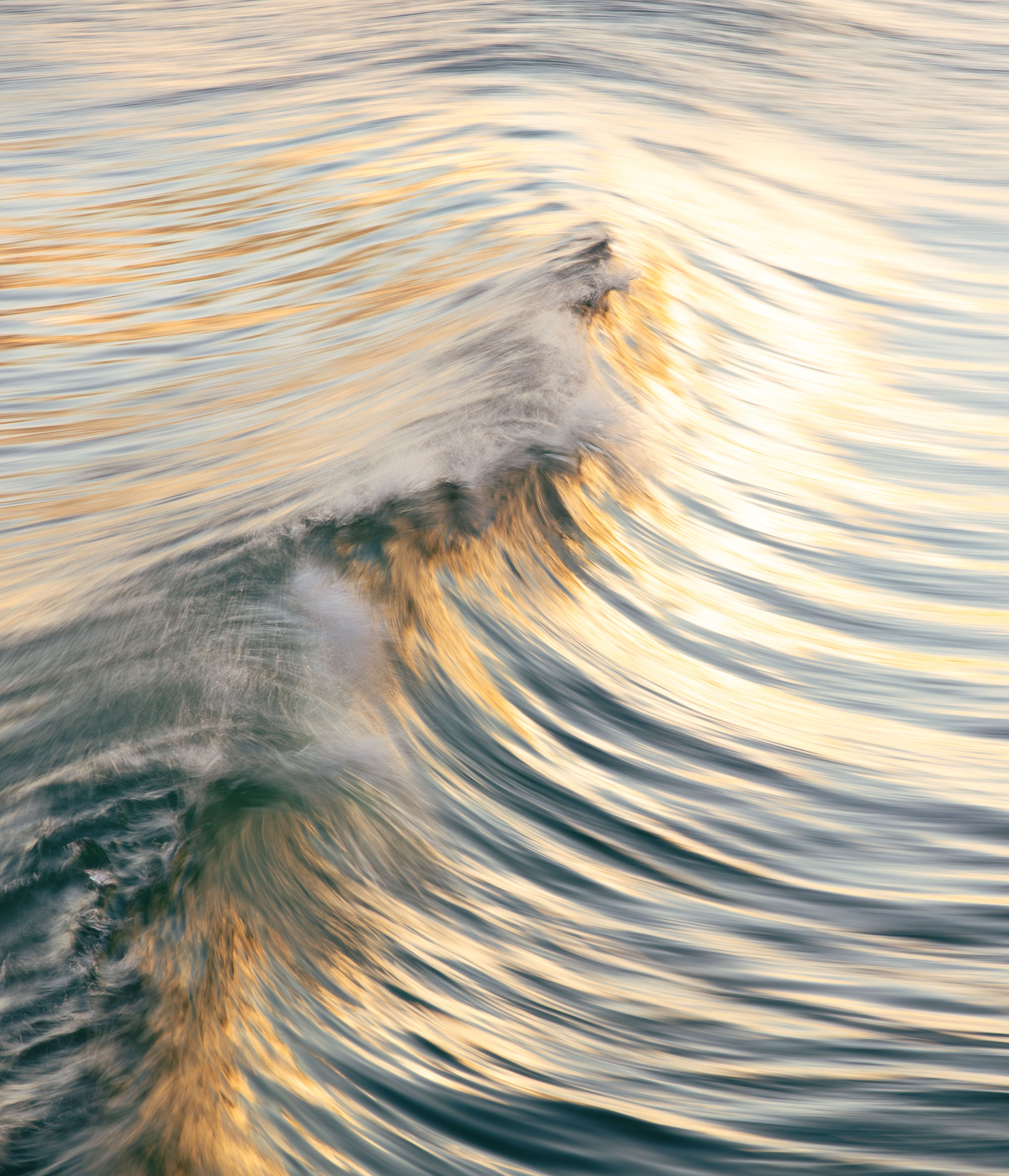 A beautiful capture of ocean waves reflecting golden sunset light with dynamic patterns.