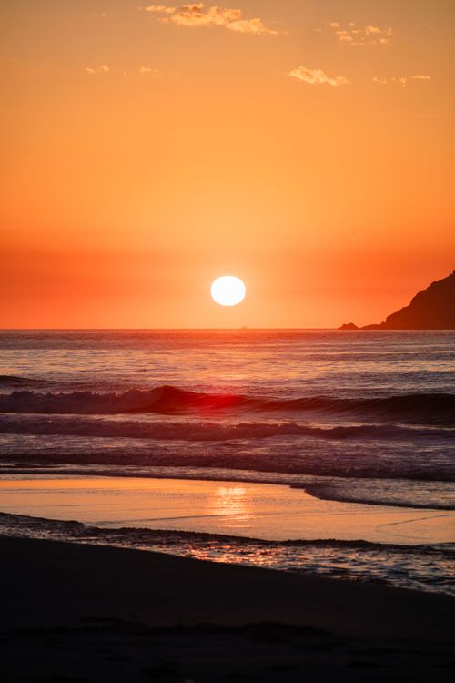 Free Breathtaking beach sunset with vibrant orange sky and setting sun over the ocean waves. Stock Photo