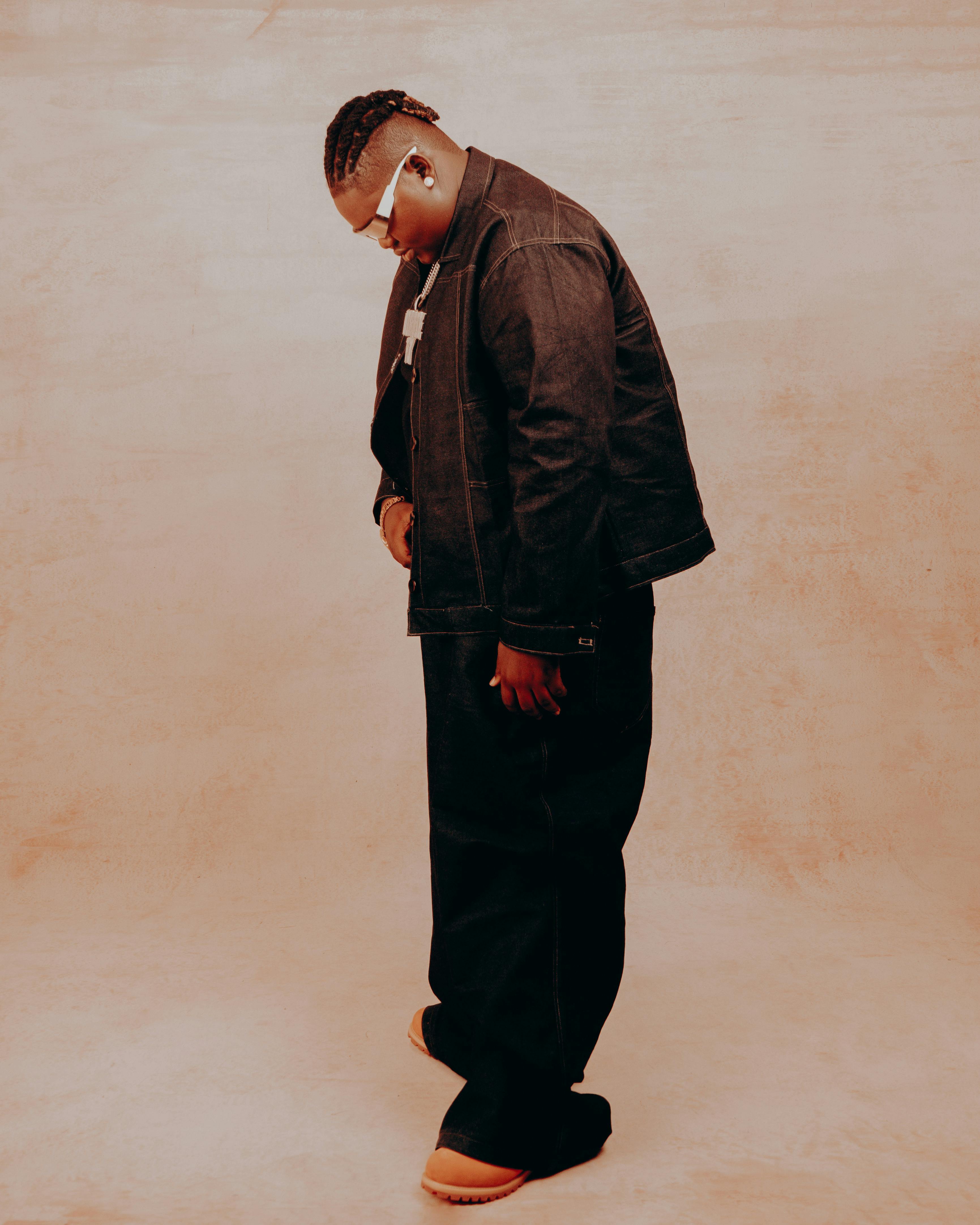 Man wearing denim jacket and pants, looking down indoors. Warm tones.