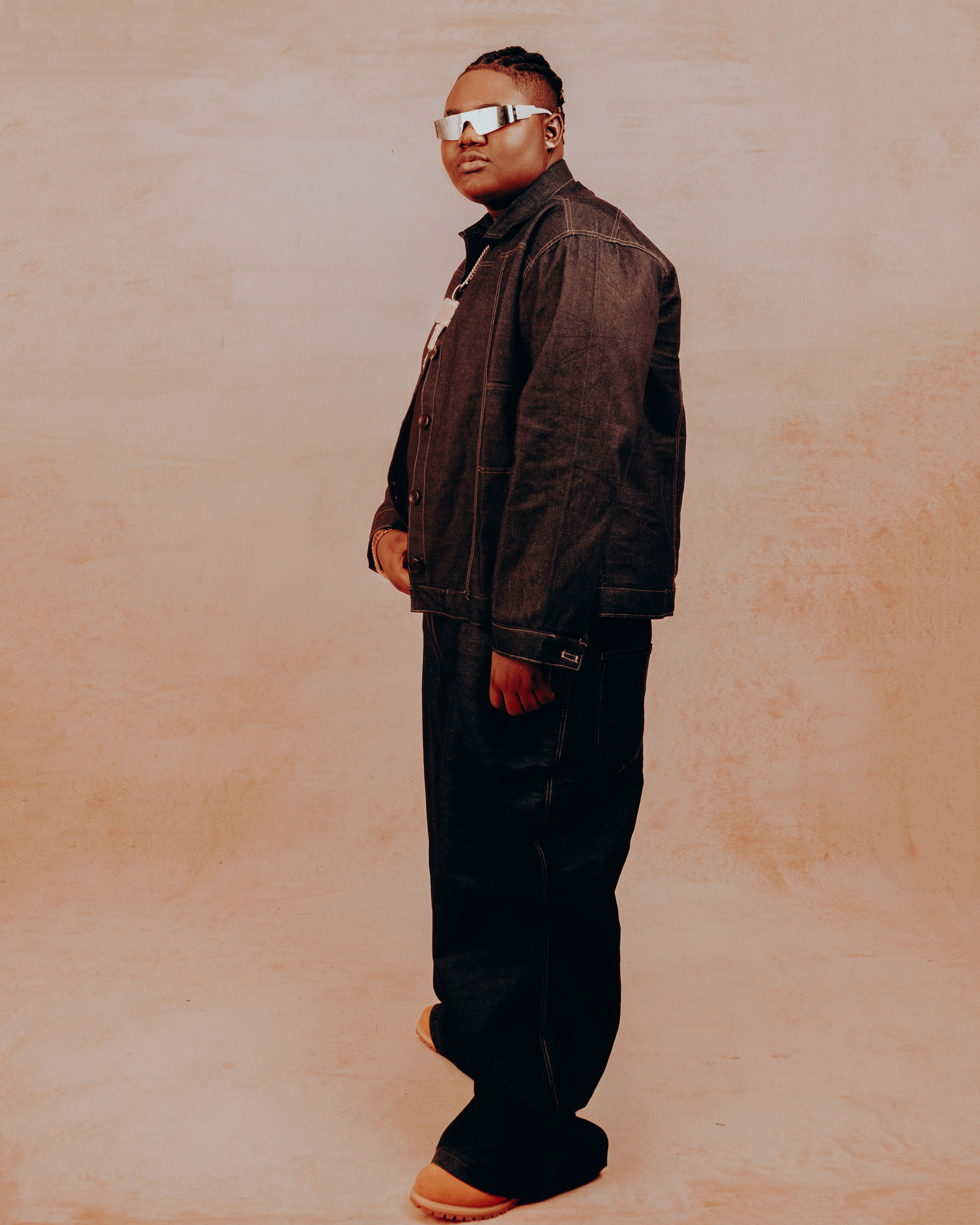 Fashionable adult wearing denim outfit and sunglasses on a warm-toned background.