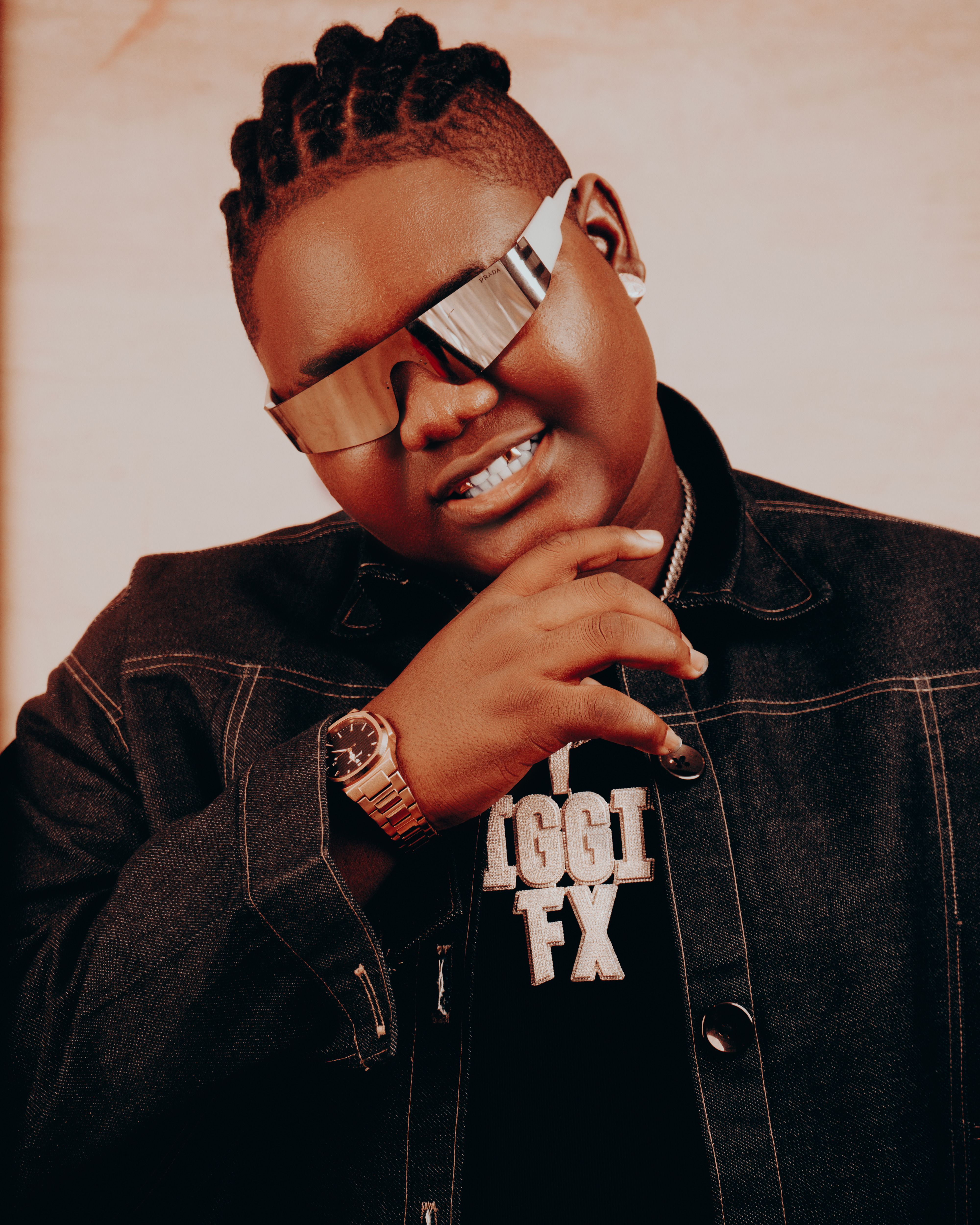 Portrait of a confident person wearing sunglasses and denim jacket against a warm backdrop.