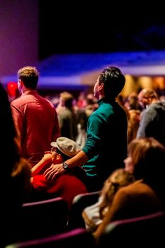 Captivated audience members watching a performance in a dimly lit indoor venue.
