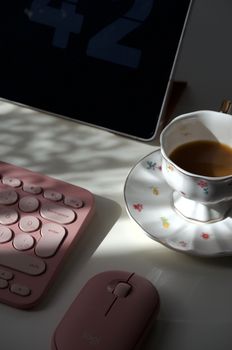 A serene workspace with a pink keyboard, mouse, and a floral coffee cup in morning light.