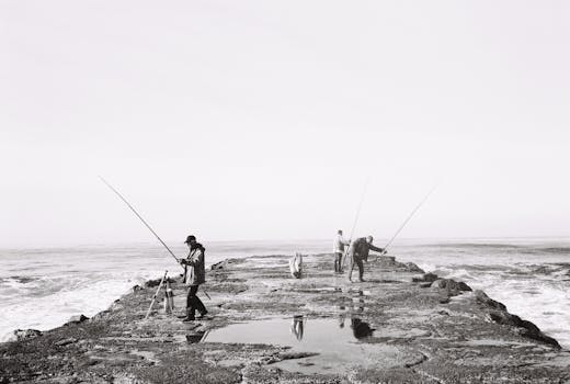 Three men fishing on a rocky pier by the sea in black and white.