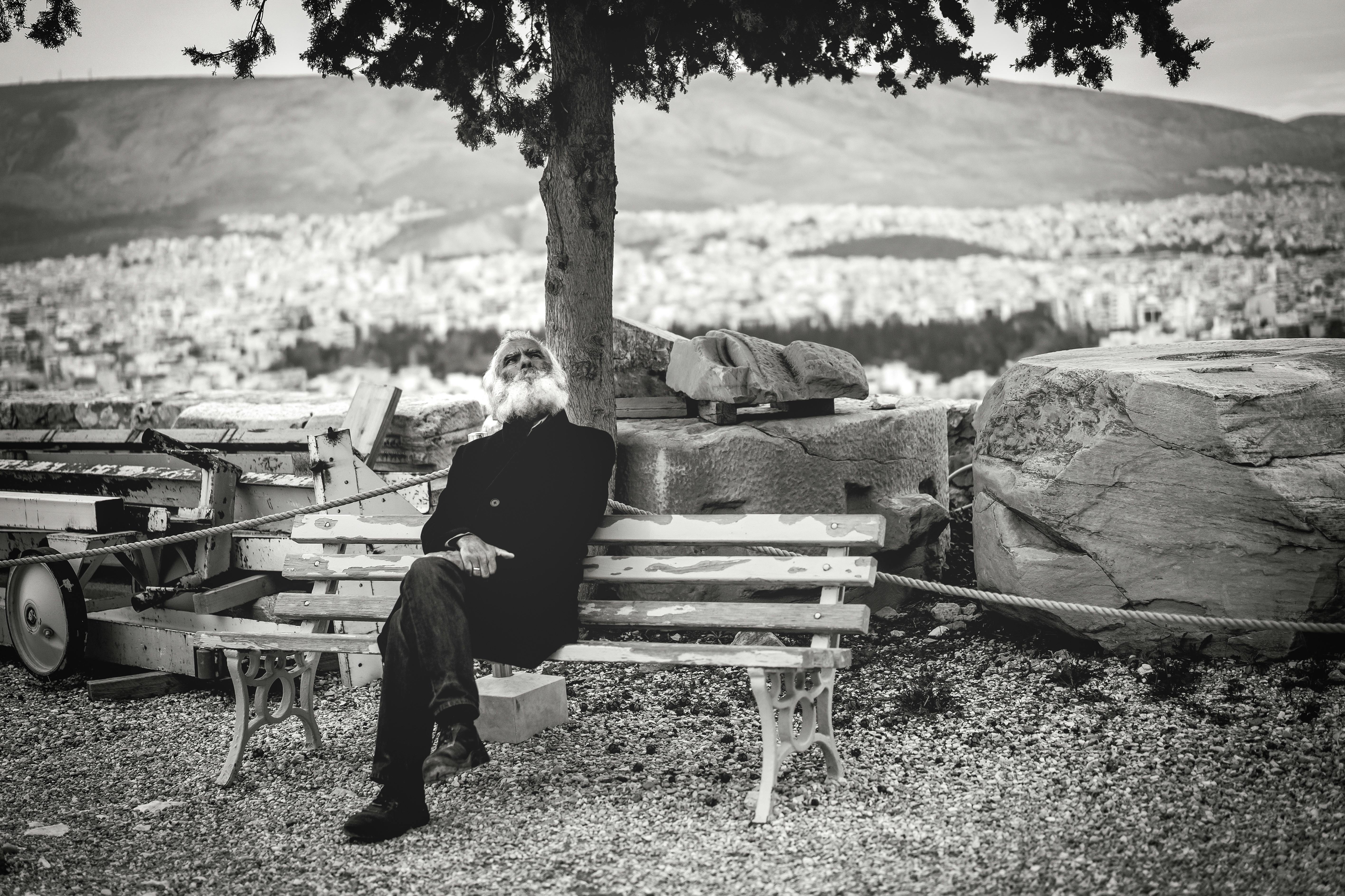 Black and white photo of an elderly man relaxing on a bench overlooking a cityscape.