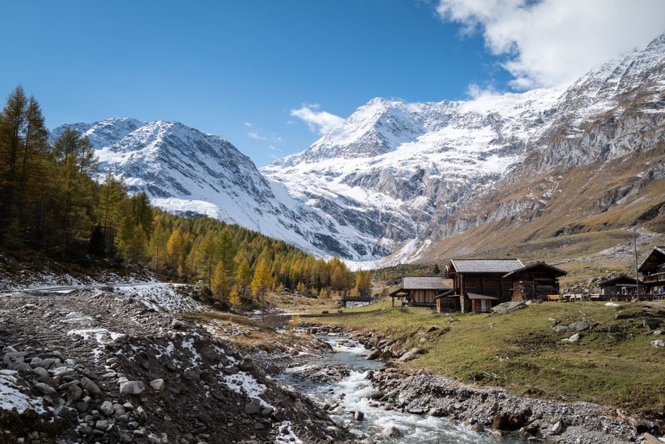 Charming alpine village with rustic cabins and snow-capped mountains under clear blue skies.