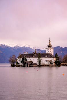 Picturesque view of Seeschloss Ort castle on Traunsee Lake with mountains in the background during twilight.